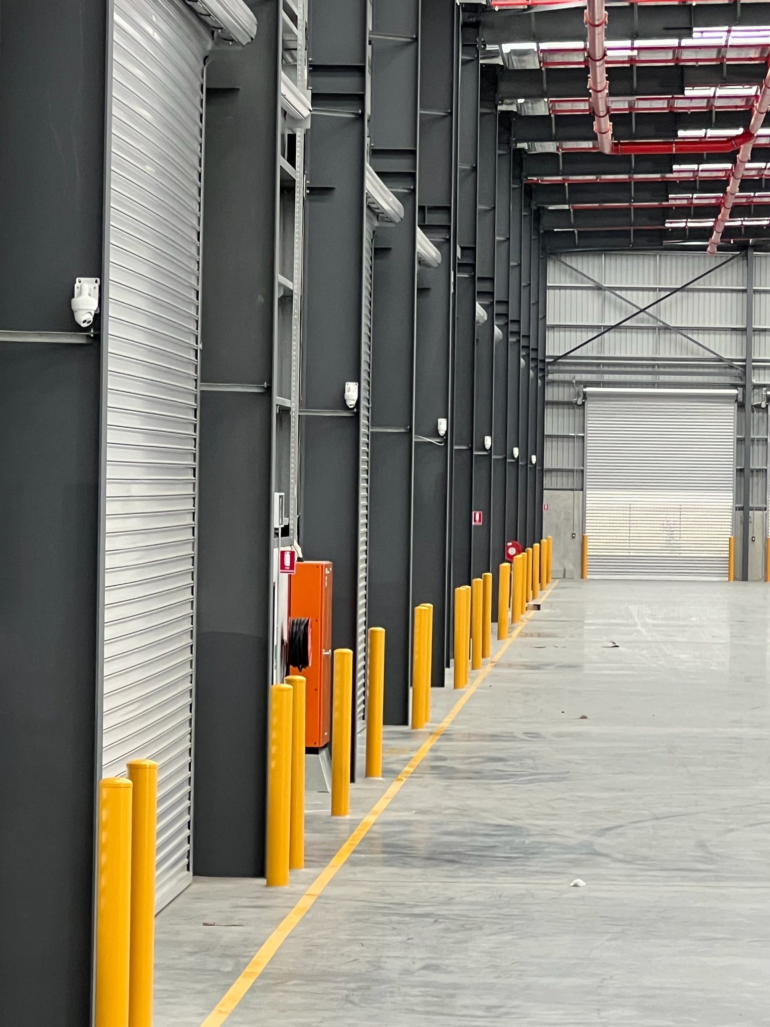 Industrial warehouse aisle with gray columns, yellow bollards, and a closed loading dock door