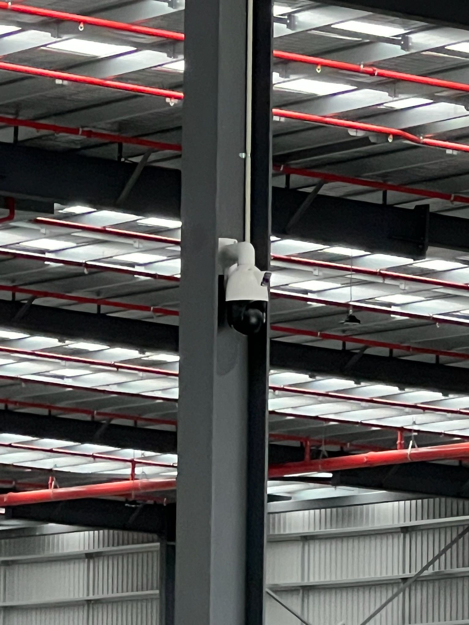 Indoor warehouse ceiling with a mounted security camera on a black support beam