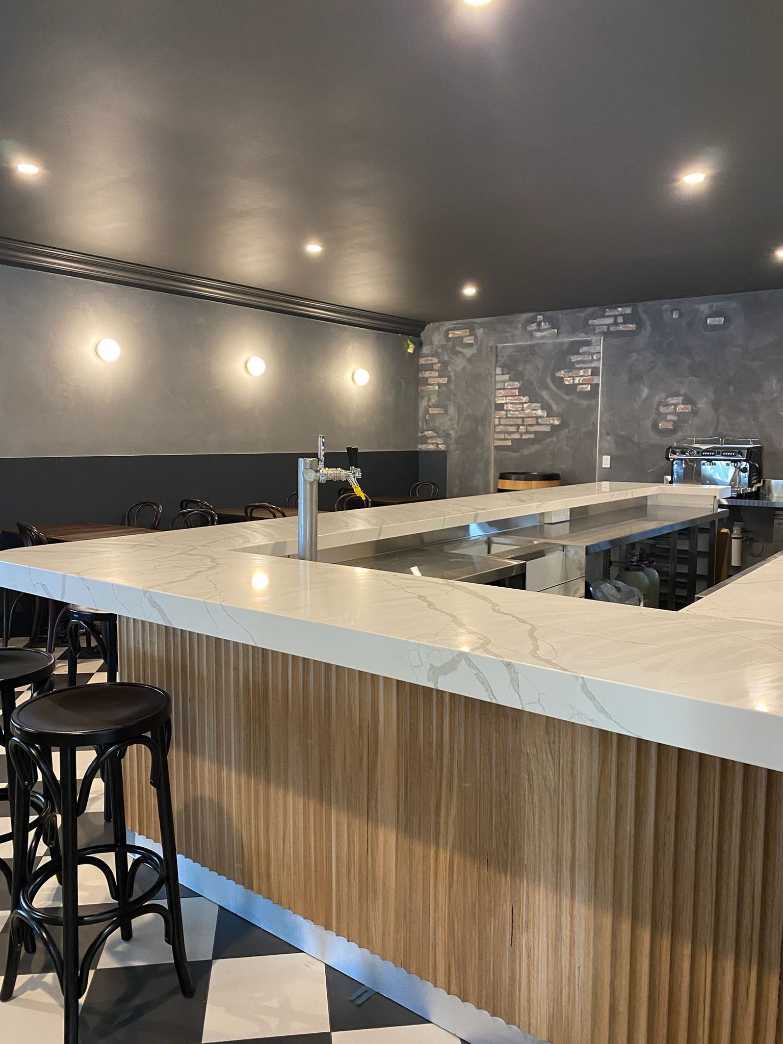 Modern bar interior with white marble counter, wood paneling, black stools, and dim ceiling lights
