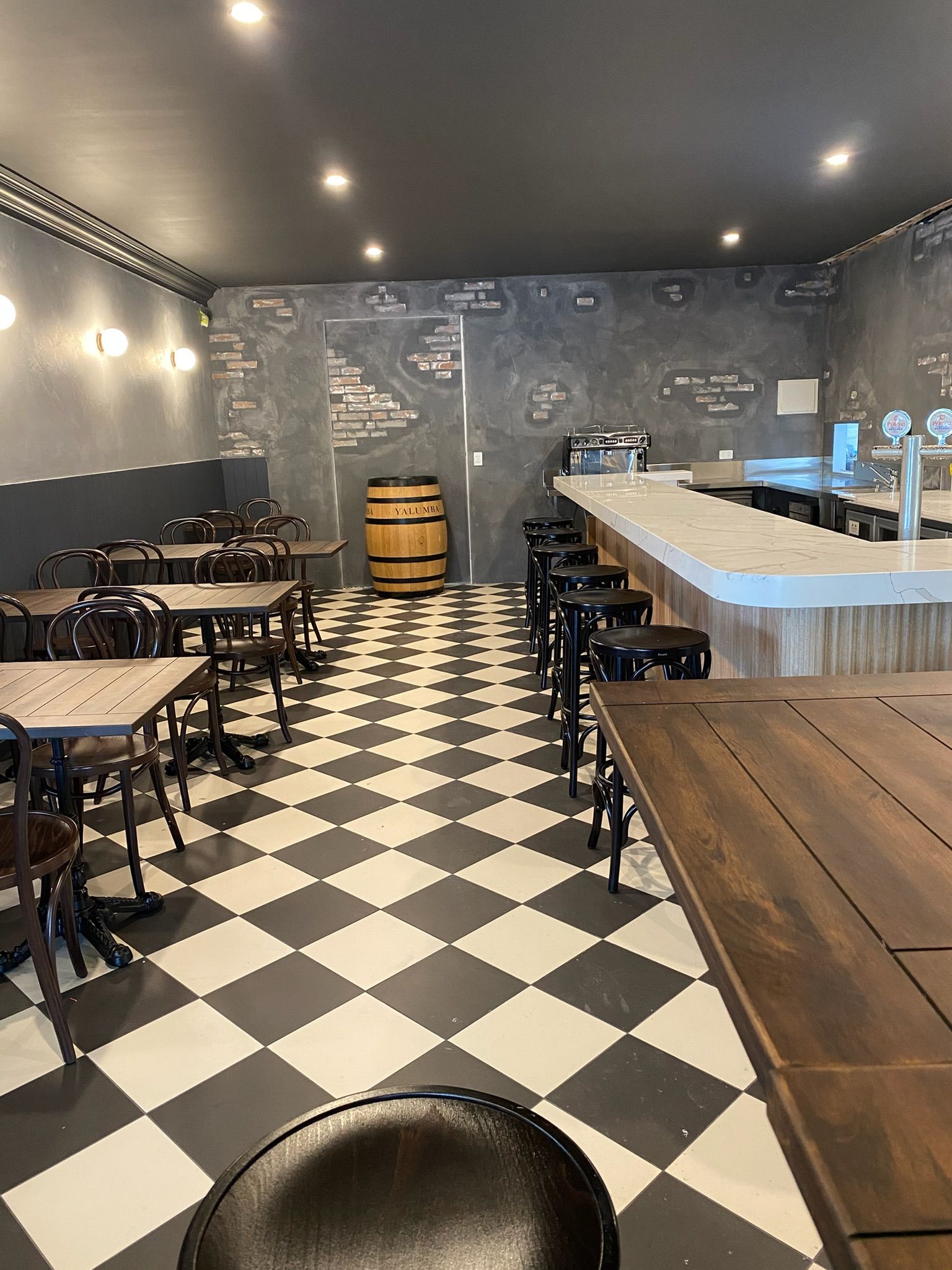 Modern café interior with black-and-white checkered floor, small tables, and a wooden bar counter