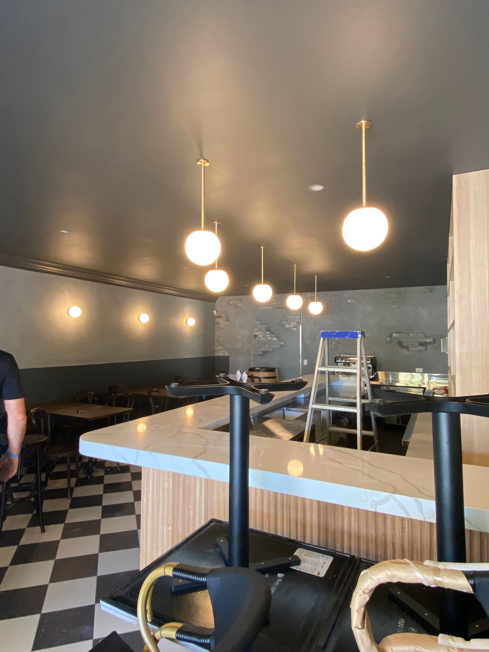 Modern café interior with pendant lights, checkered floor, bar counter, and ladder in back