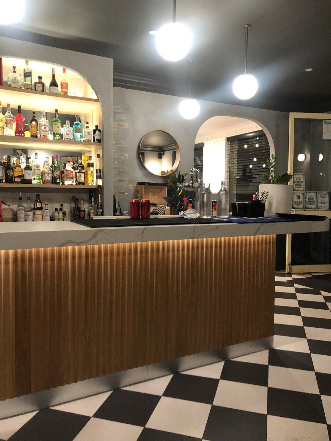 Modern bar interior with backlit shelves, arched openings, and a black-and-white checkered floor