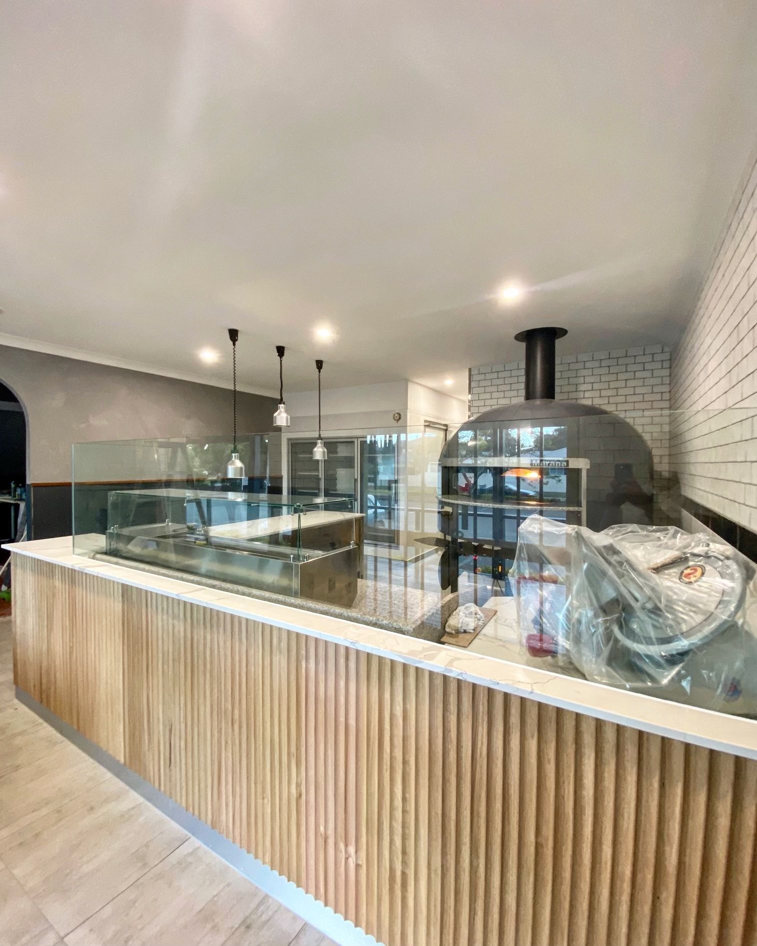 Modern bakery counter with glass display cases, wood front, and brick oven in a bright interior