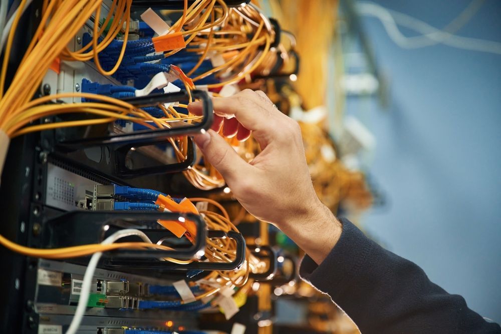 Hand connecting orange network cables in a server rack