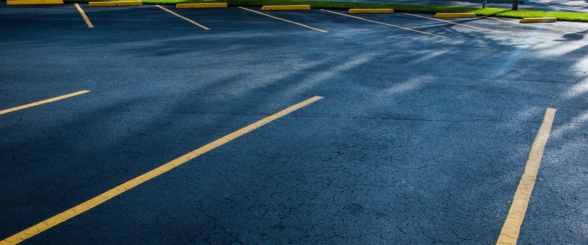 Asphalt parking lot with yellow parking lines and concrete stops.