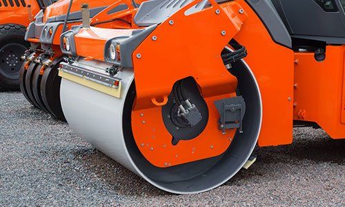 Orange and gray road roller compacting gravel.