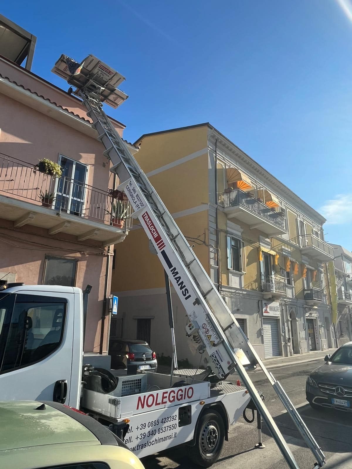 davanti a un edificio è parcheggiato un camion bianco con una scala fissata sul retro.