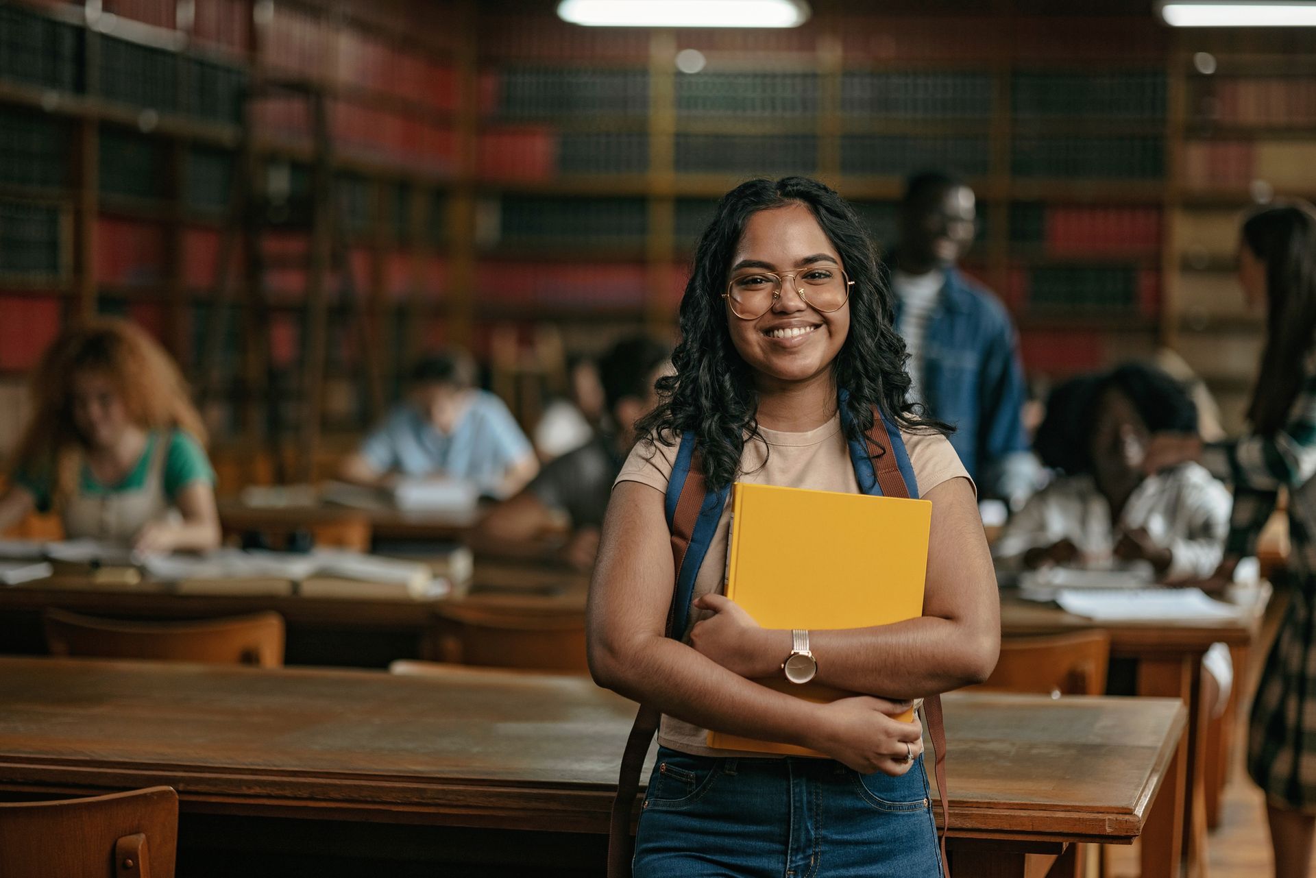 A woman is standing in a library holding a book and smiling.