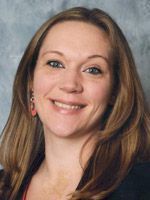 Man smiling in a blue striped shirt and yellow tie, wearing a dark suit jacket, business setting.