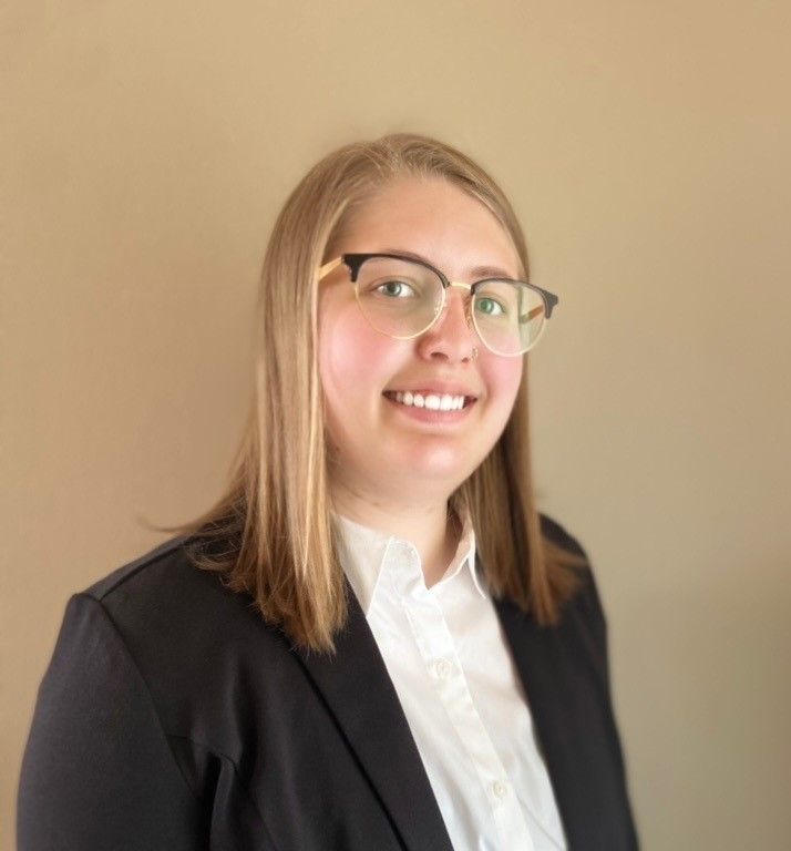 Man smiling in a blue striped shirt and yellow tie, wearing a dark suit jacket, business setting.