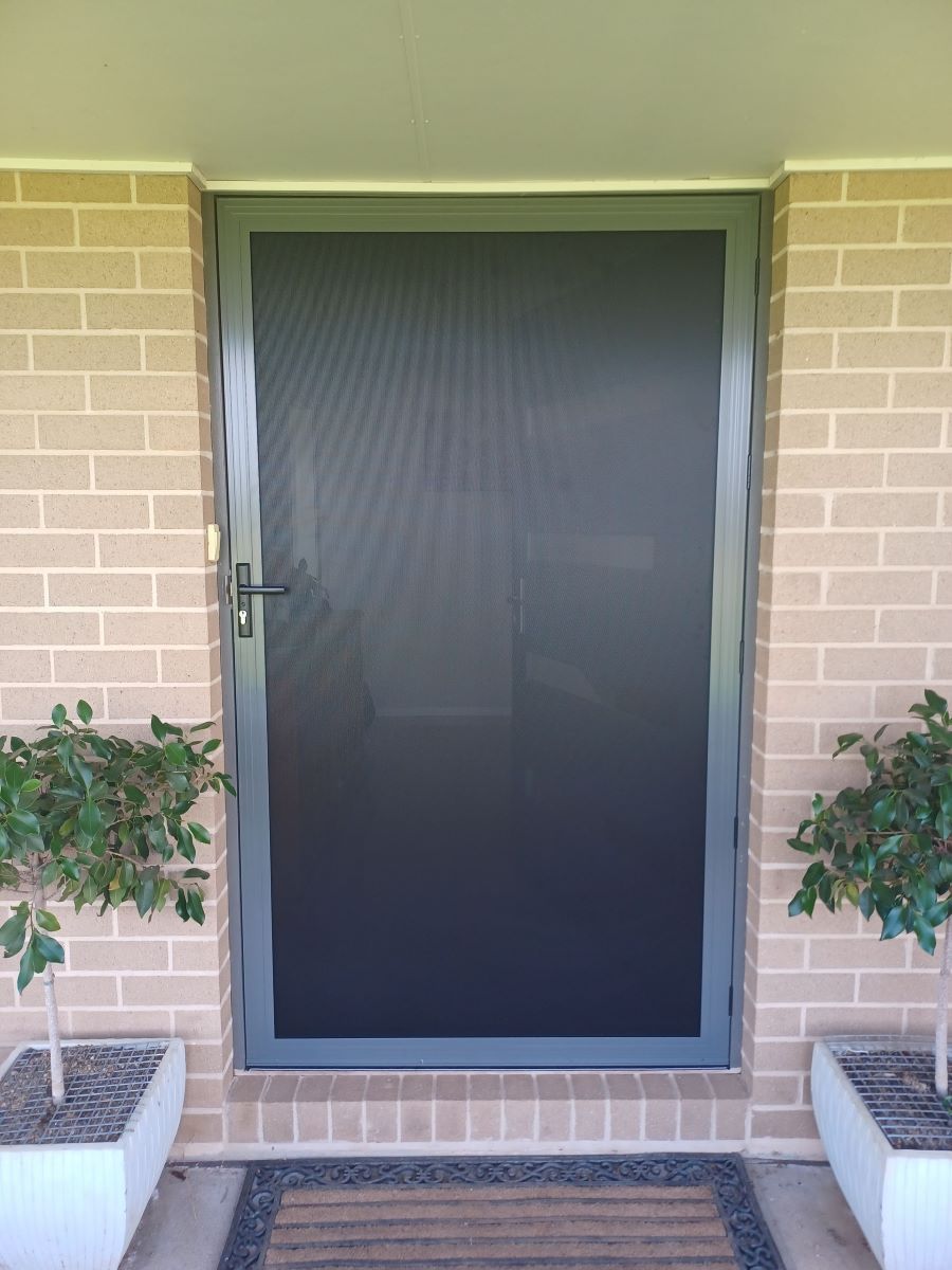 A Black Screen Door is Sitting on a Brick Wall — BTS Blinds & Awnings in Gunnedah, NSW