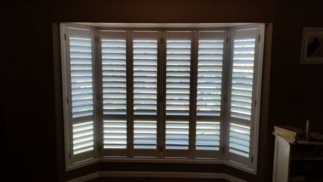 A Large Bay Window With White Shutters in a Dark Room — BTS Blinds & Awnings in Gunnedah, NSW