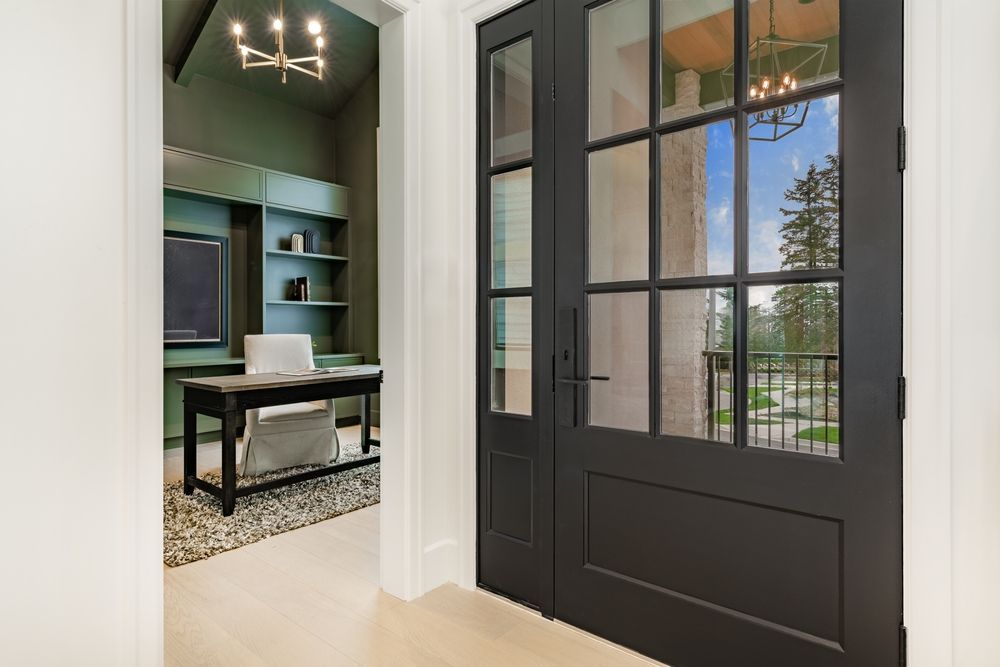 Black French doors leading to a green office space with desk, shelving, and outdoor view.