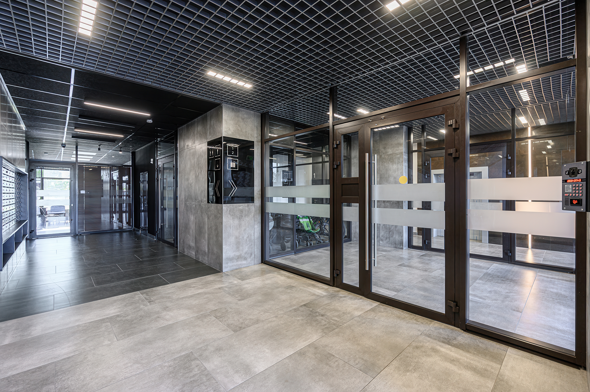 Modern office hallway with glass doors, gray walls, and tiled floor; grid ceiling.
