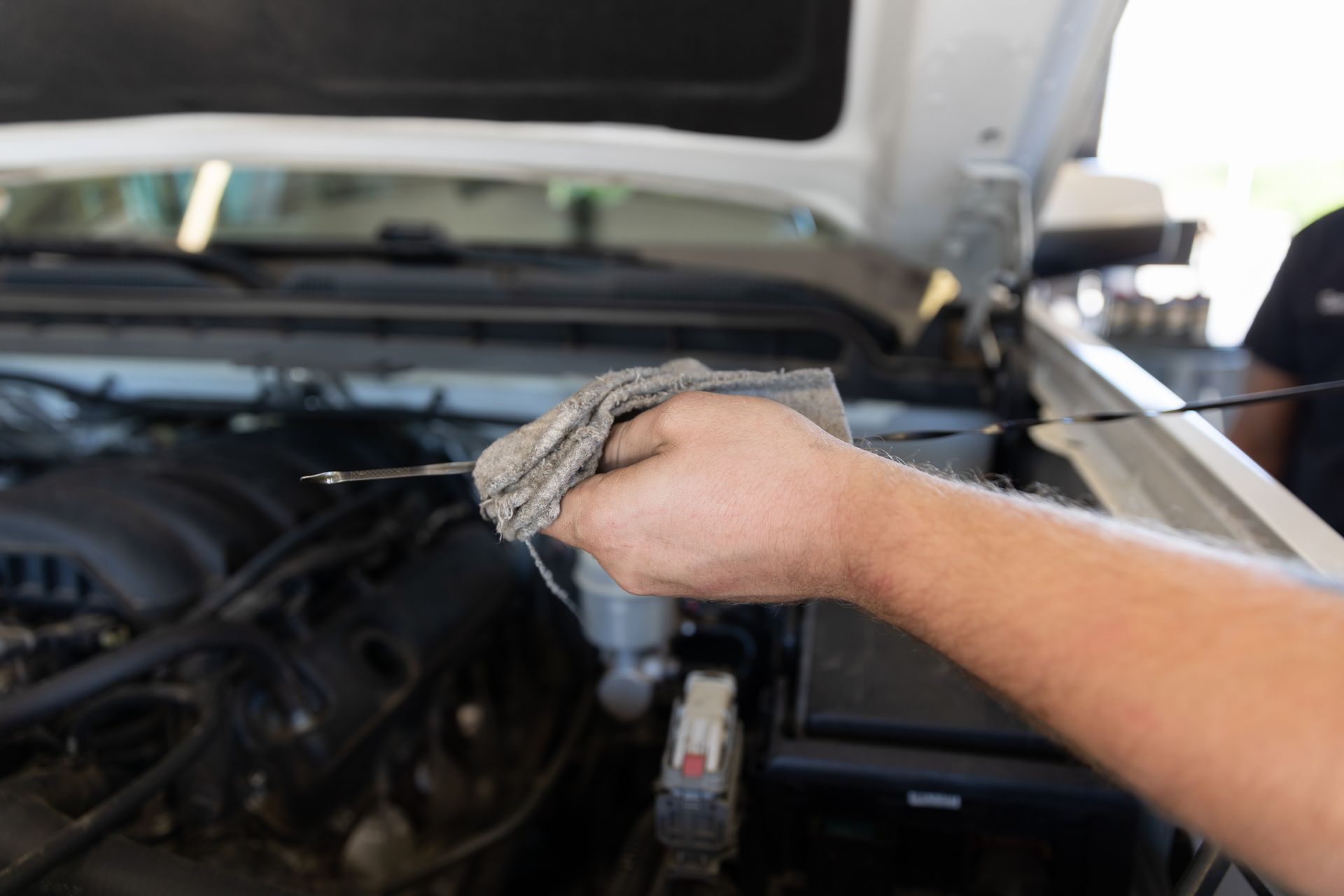 A person is cleaning the engine of a car with a cloth.