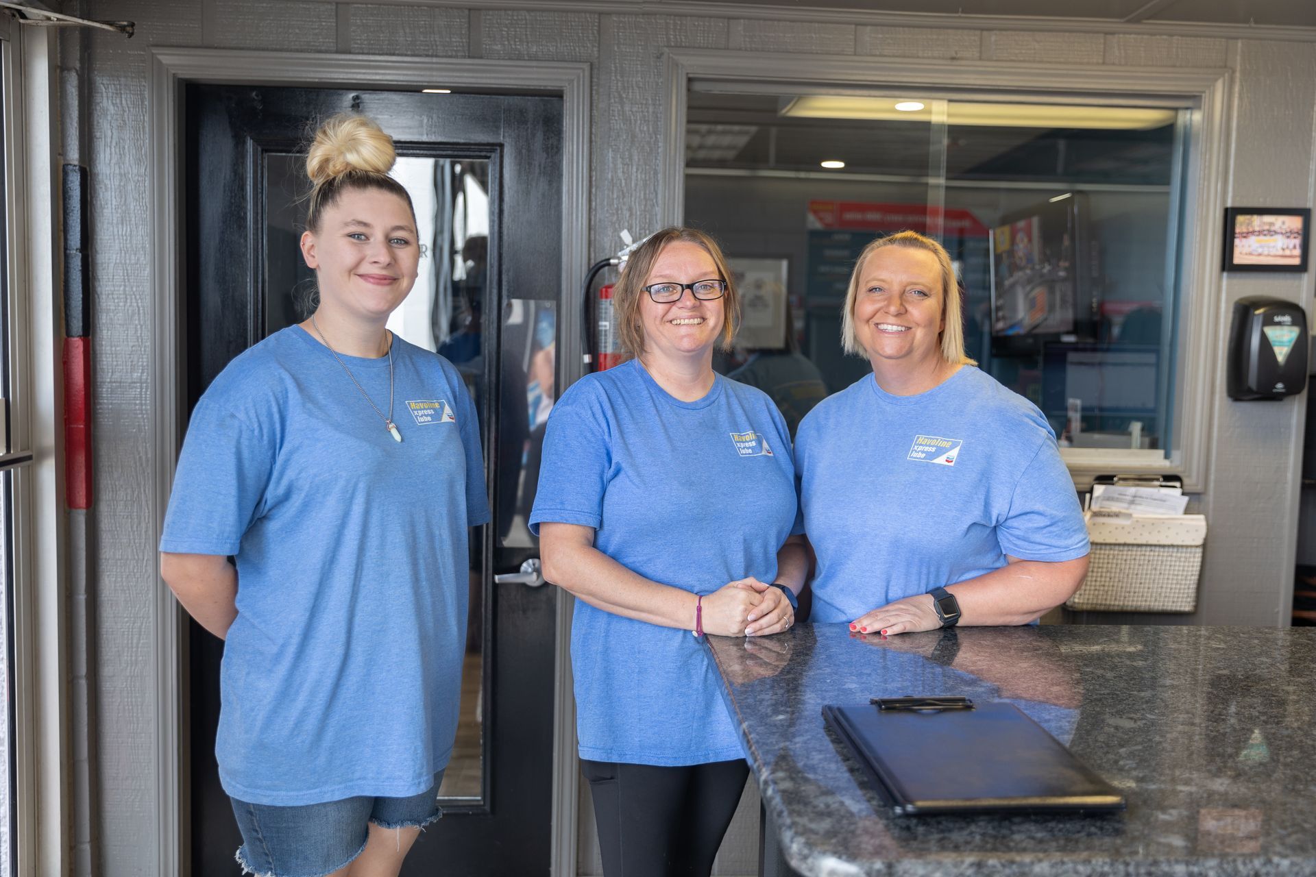 Three women in blue shirts are standing next to each other in front of a counter.