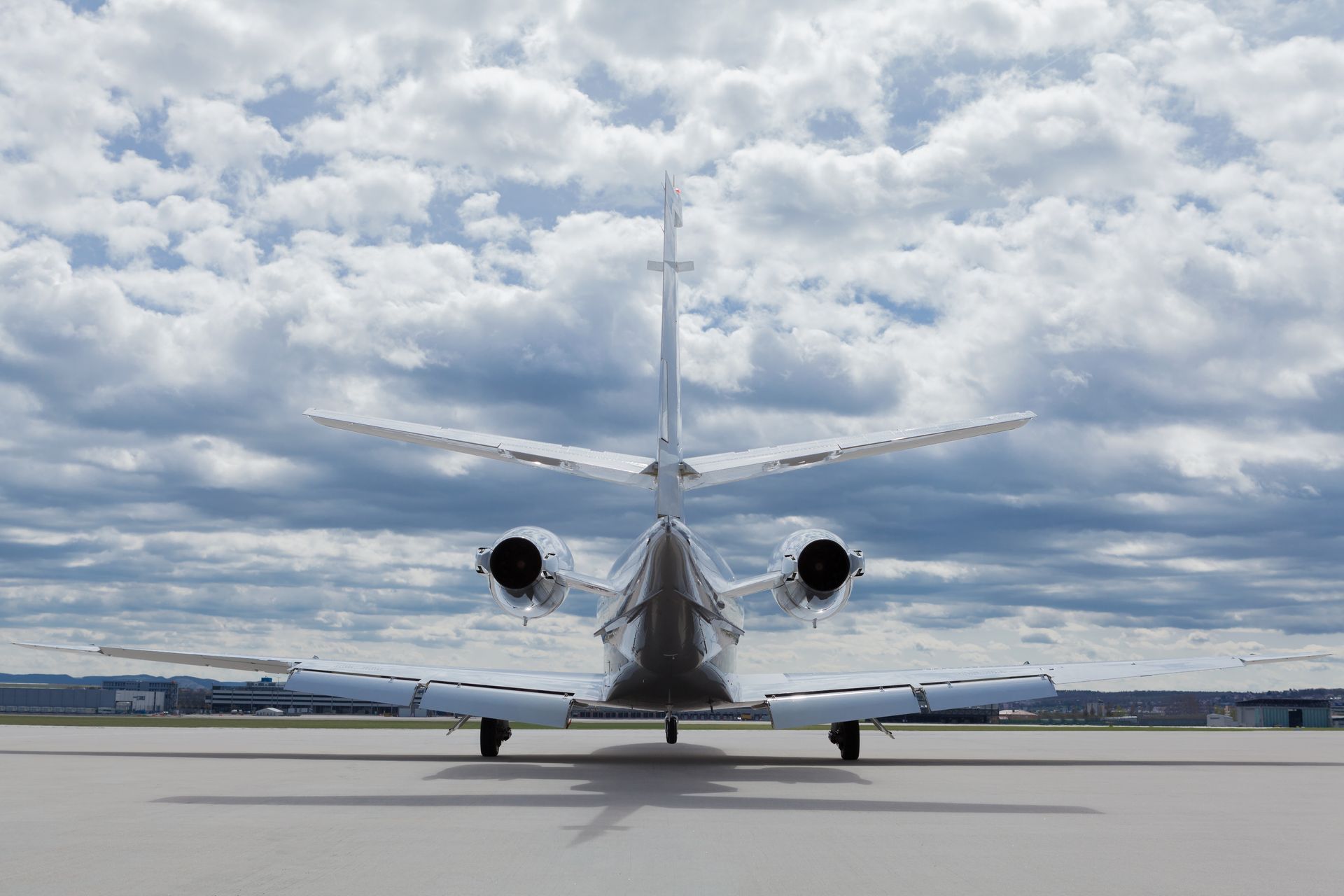 Rear view of a silver private jet on a tarmac under a cloudy sky.