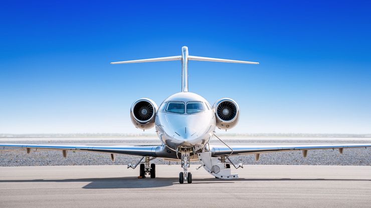 Silver private jet on a tarmac, blue sky background.