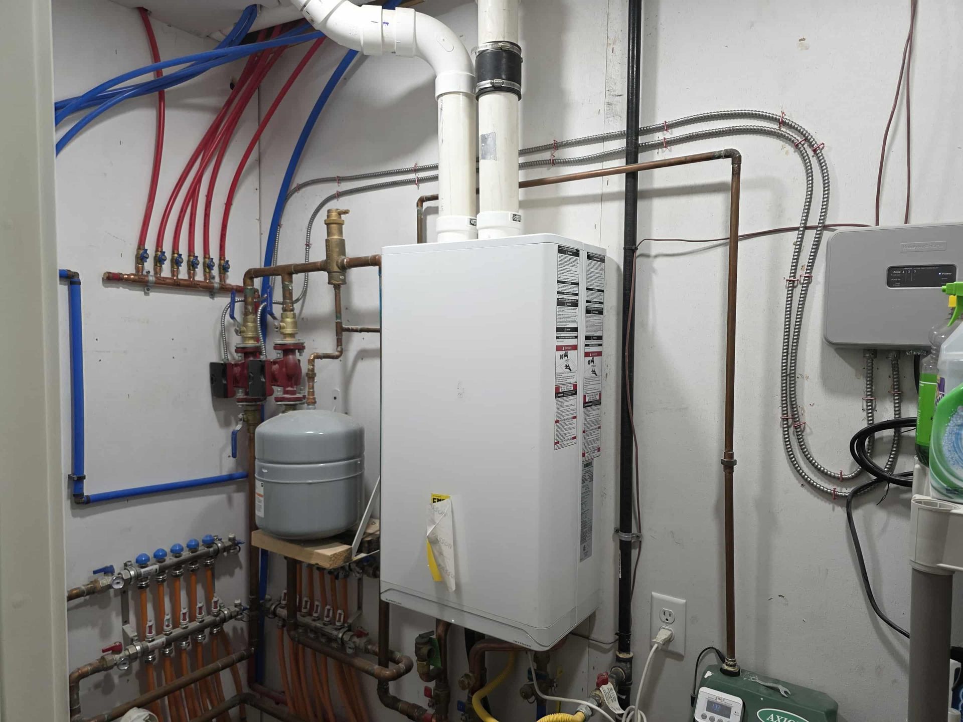 White water heater with pipes in a utility room. Blue and red pipes connect to a manifold.