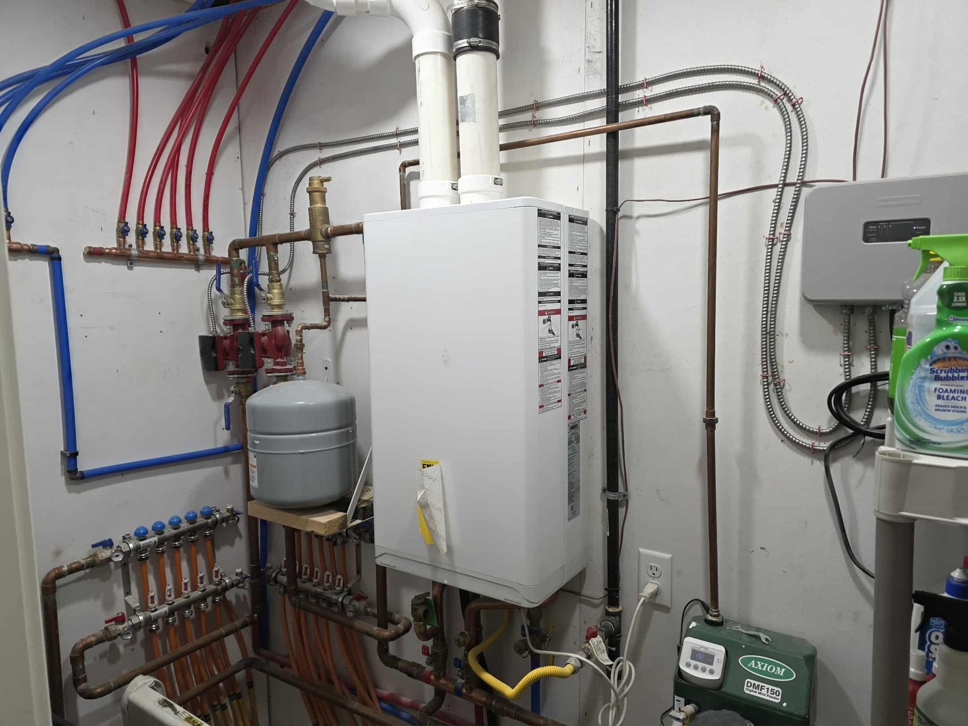 Water heater and plumbing system in a utility room. Pipes are red, blue, and copper. White walls.