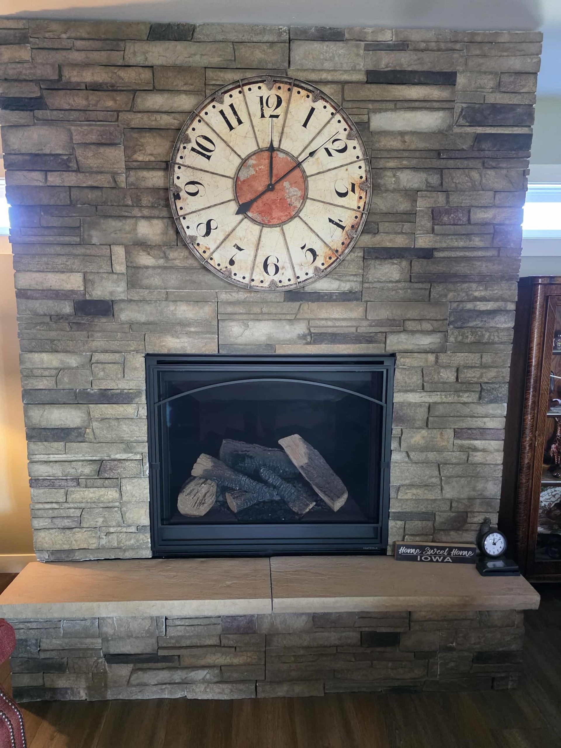 Fireplace with stone facade, a clock above. Brown logs sit inside the fireplace.