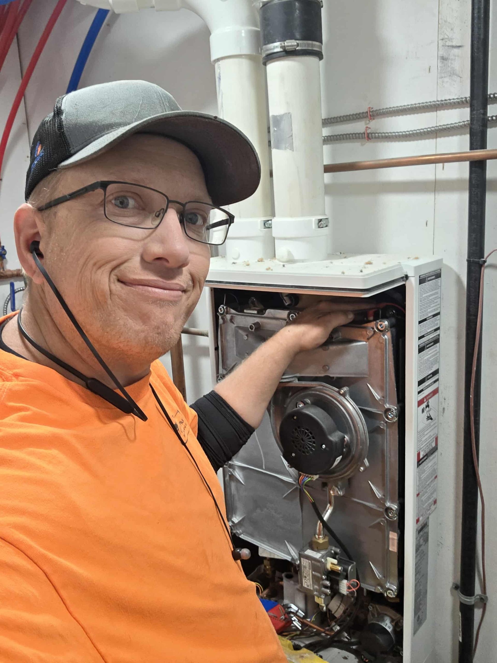 Man in orange shirt with glasses, working on a water heater, indoors.