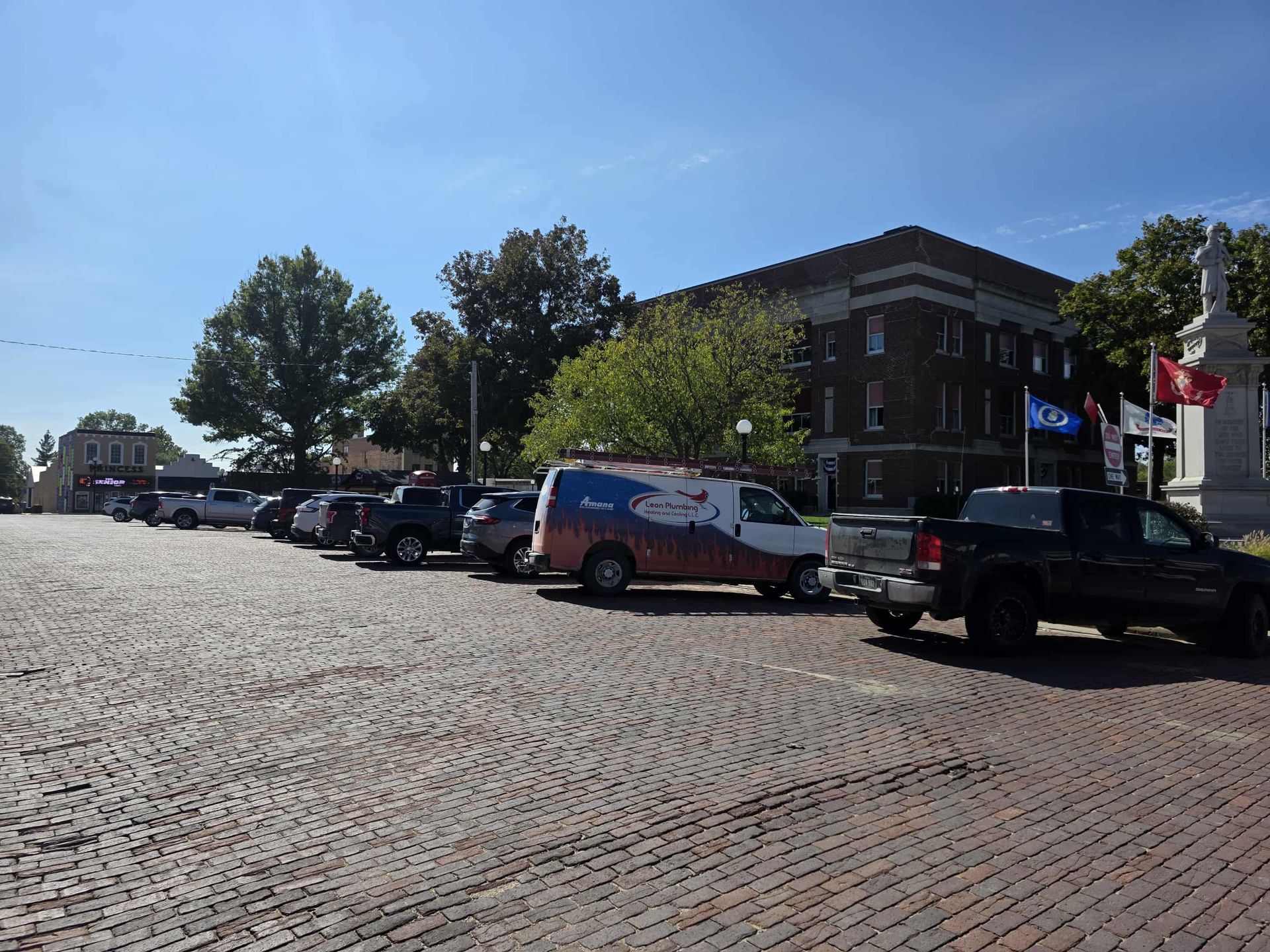 Cars parked on brick street in front of a large brick building under a blue sky.