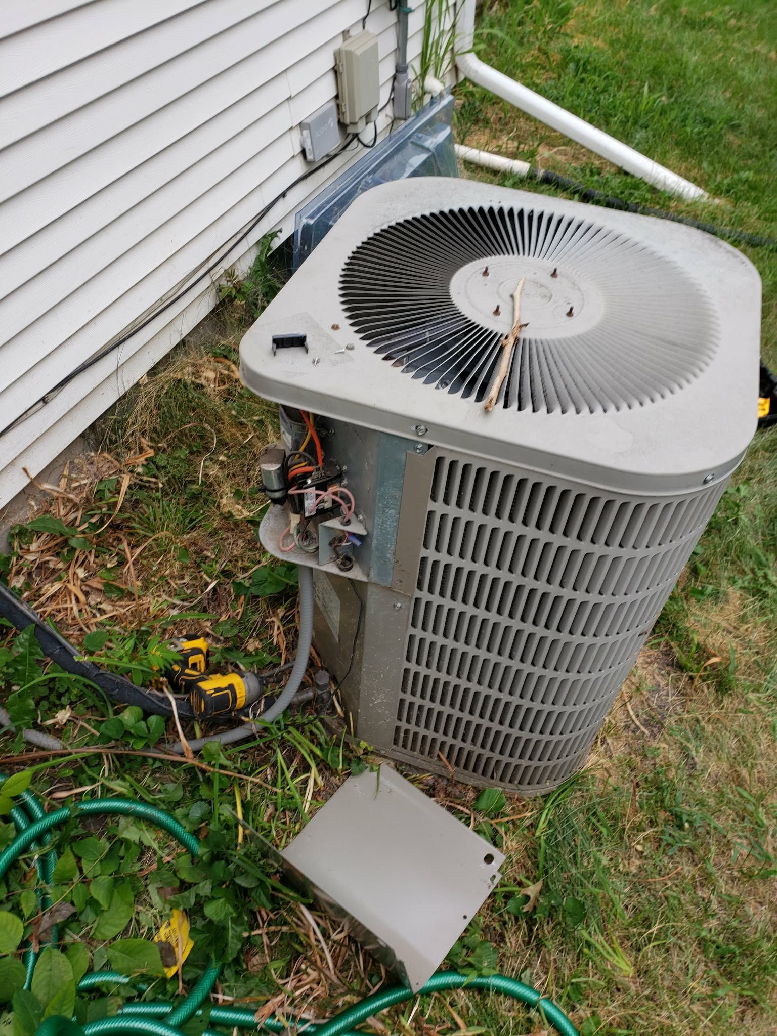 Outdoor air conditioning unit with open panel, next to a house on a grassy lawn.
