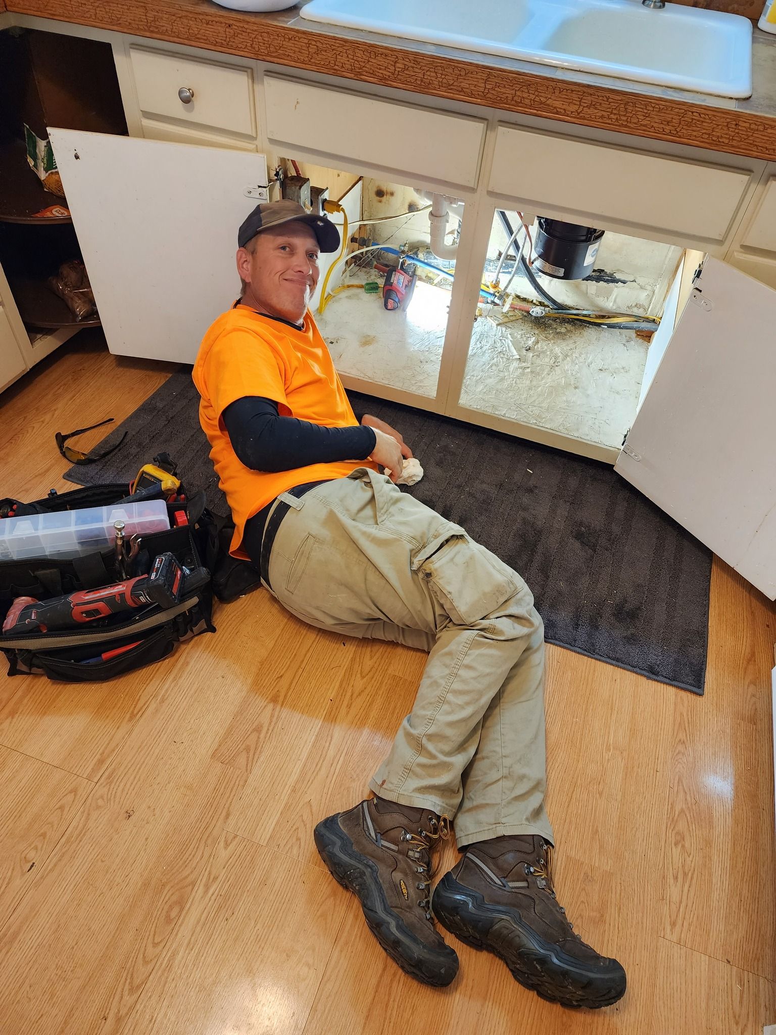 Plumber's hand with wrench fixing a leaking pipe. Water spraying against a dark brown wall.