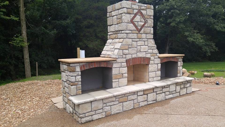 A large stone fireplace is sitting on top of a gravel driveway.