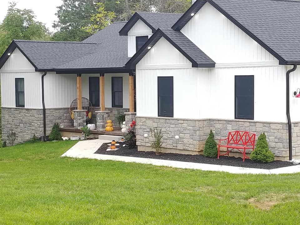 A white house with a black roof and a red bench in front of it.