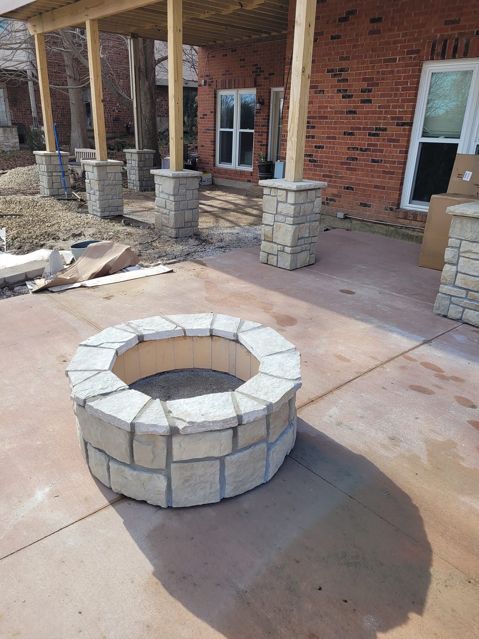 A fire pit is sitting on a concrete patio in front of a brick house.