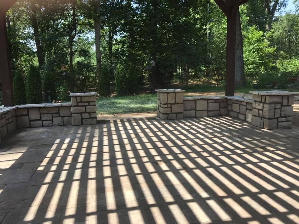 A stone patio with a pergola and trees in the background.