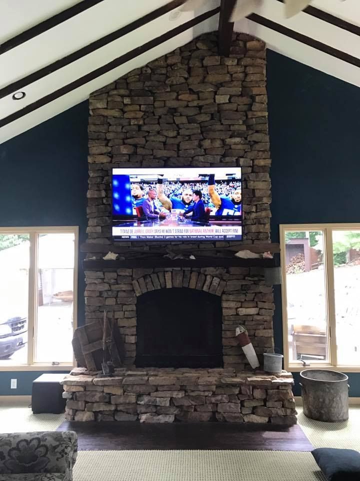 TV mounted above a fireplace, flanked by windows. The room has high ceilings with dark beams and dark blue walls.