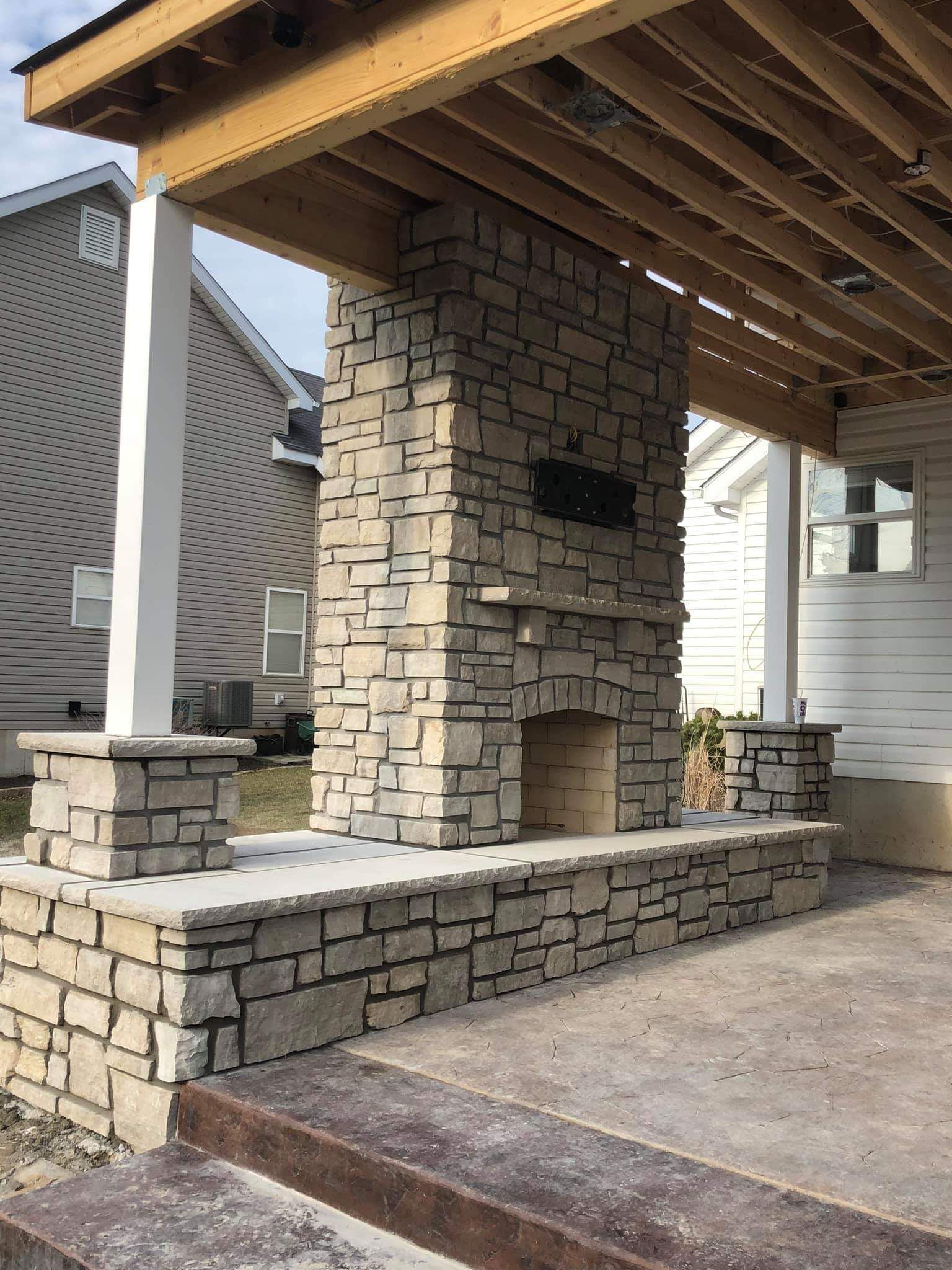 A large stone fireplace is under a covered patio.