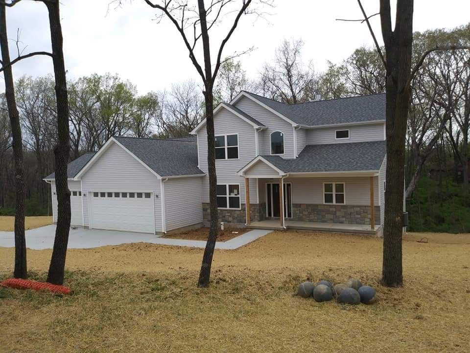 A white house with a gray roof is surrounded by trees