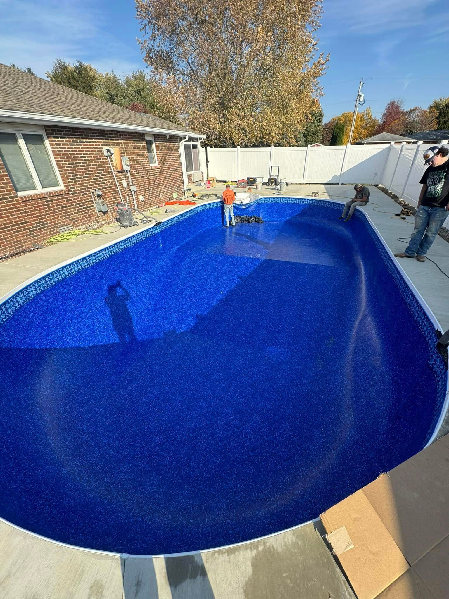 A large blue swimming pool is being built in the backyard of a house.