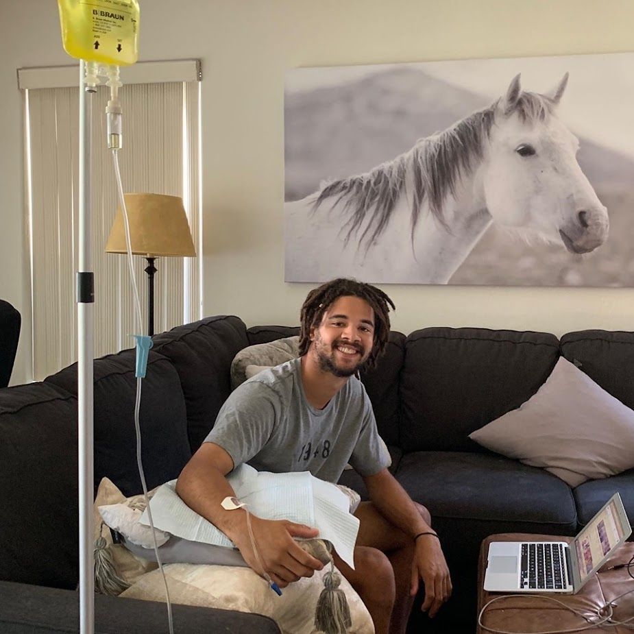 A man is sitting on a couch with IV drips, in front of a picture of a horse