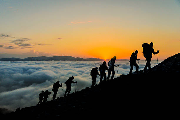A group of people are hiking up a mountain at sunset.