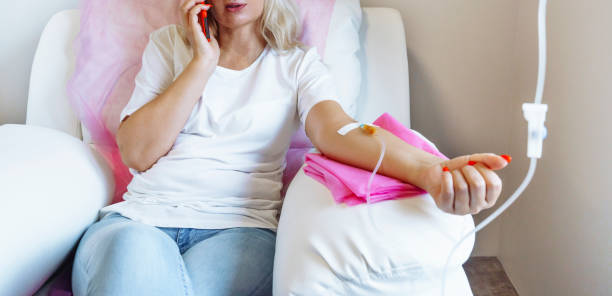 A woman is sitting on a couch with an iv in her arm and talking on a cell phone.