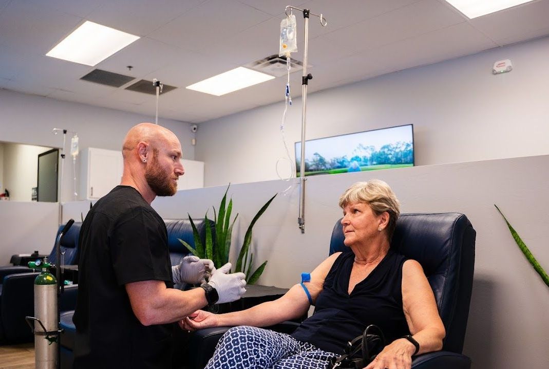 A man is kneeling down preparing the IV next to a woman in a chair.