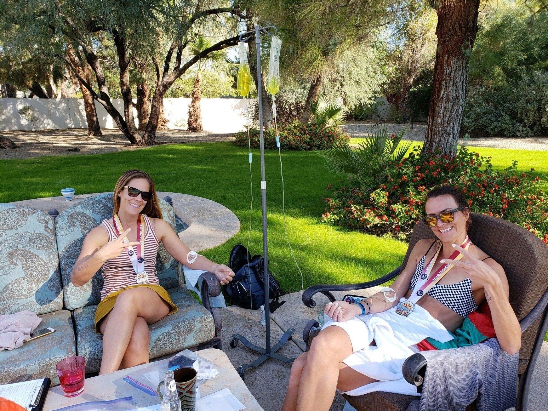 Two women are sitting on a couch in a park.