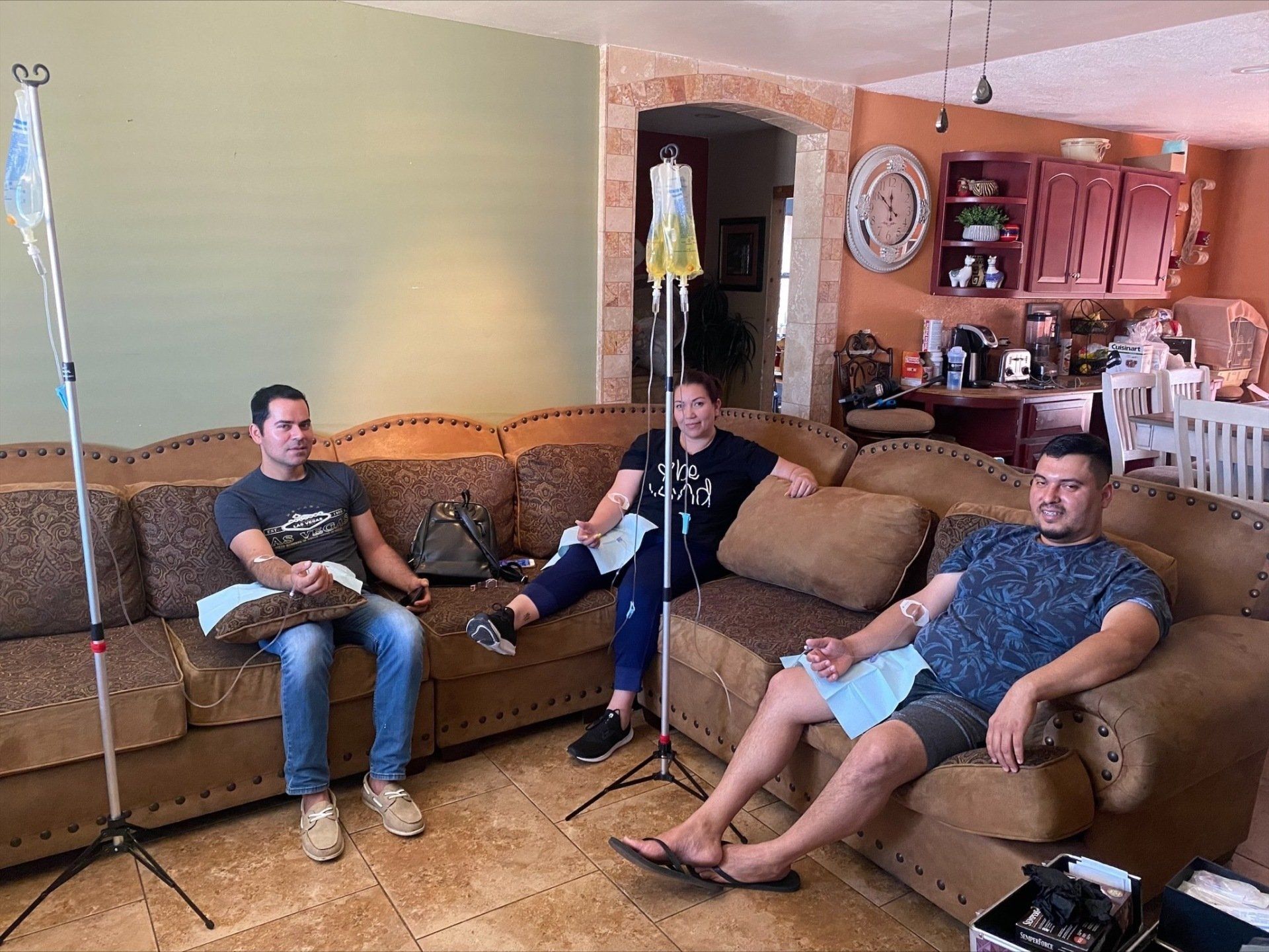 Group of 3 people sitting on a couch with IV on their arm.