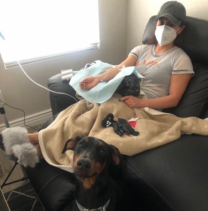 A woman wearing a mask is sitting on a couch next to a dog