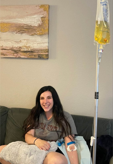 A woman is sitting on a couch with an iv in her arm.