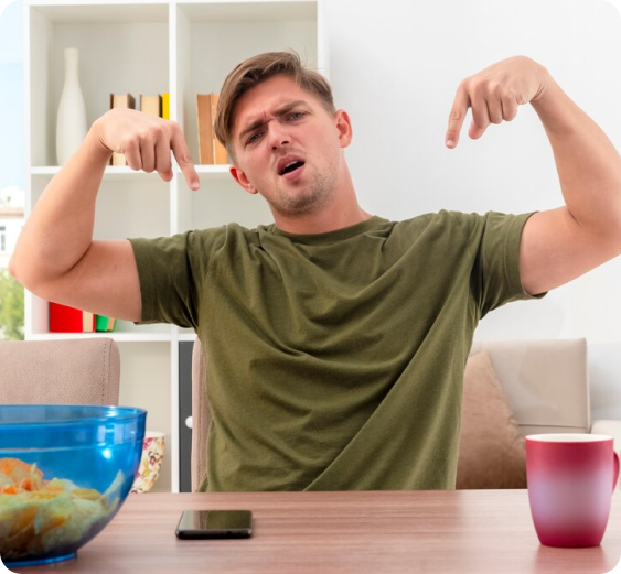 A man in a green shirt is sitting at a table flexing his muscles