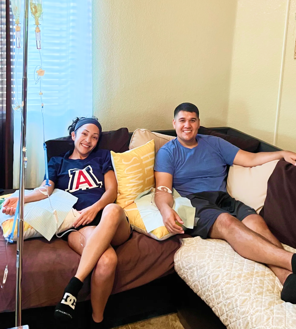 A woman is sitting on a couch with a blue bandage on her arm.