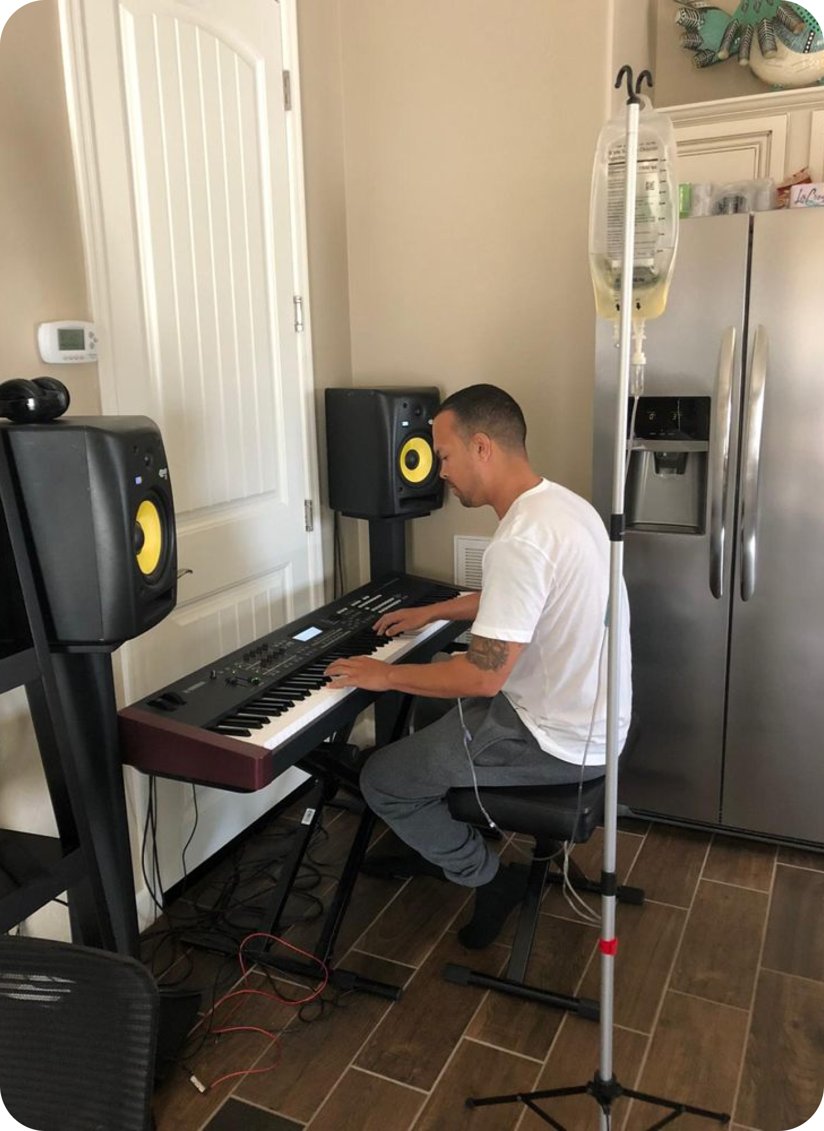 A man is sitting in a chair playing a keyboard in a kitchen.