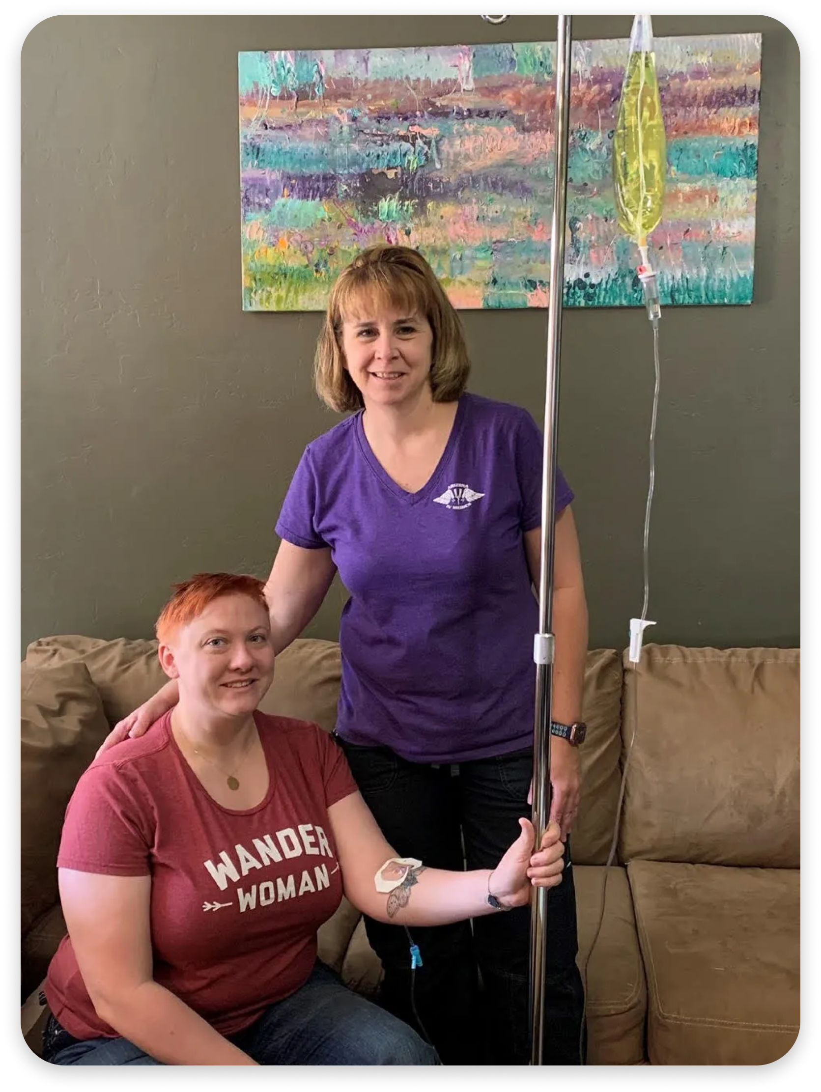 Two women are sitting on a couch with an iv in their arm.
