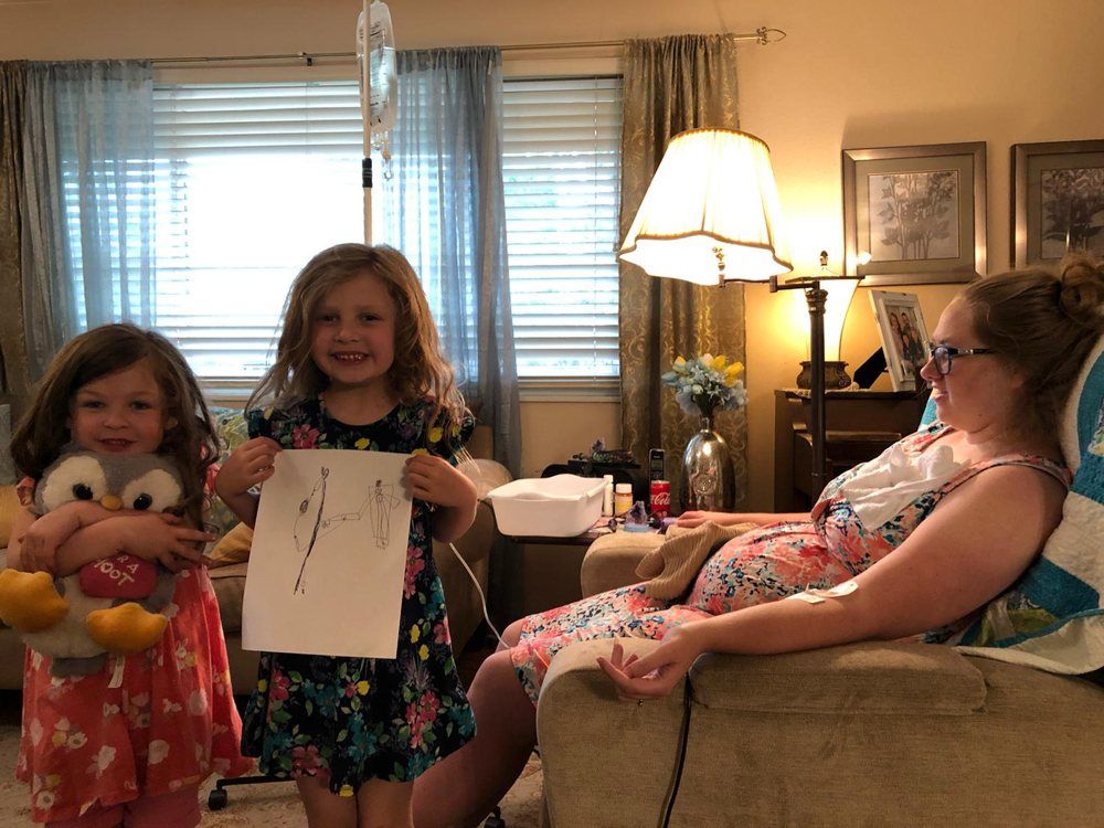 Two little girls are standing next to a pregnant woman in a living room.